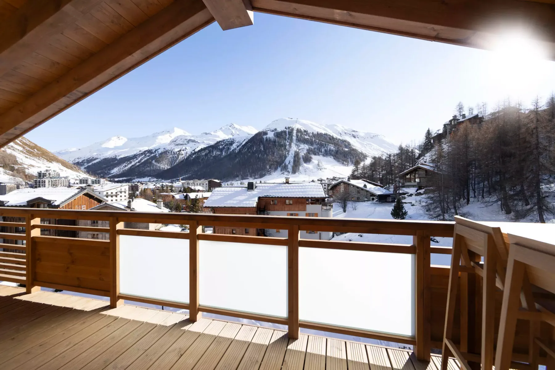 A wooden balcony overlooks a snow-covered mountain village and surrounding peaks.