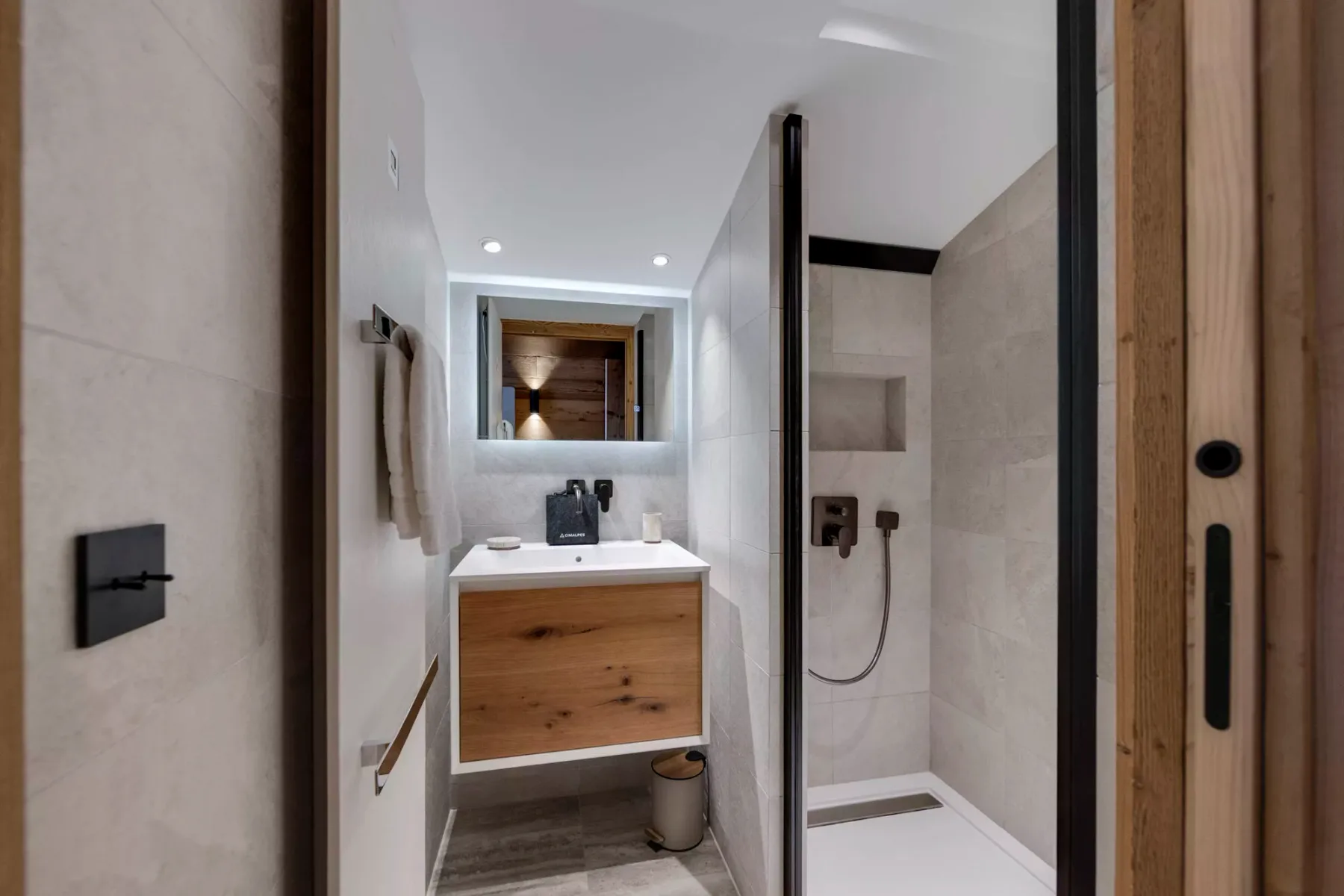 A tiled bathroom with a wood-front vanity, mirror, and shower.