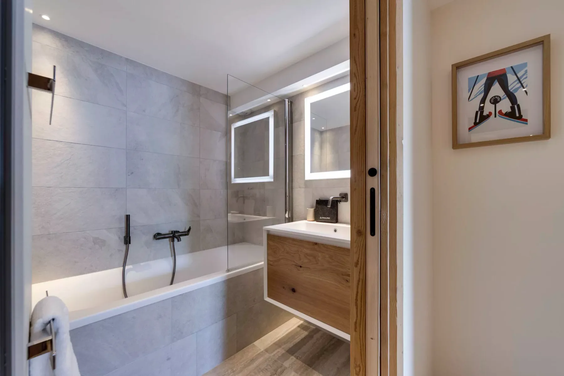 A modern bathroom with a bathtub, shower fixtures, and a wood vanity.