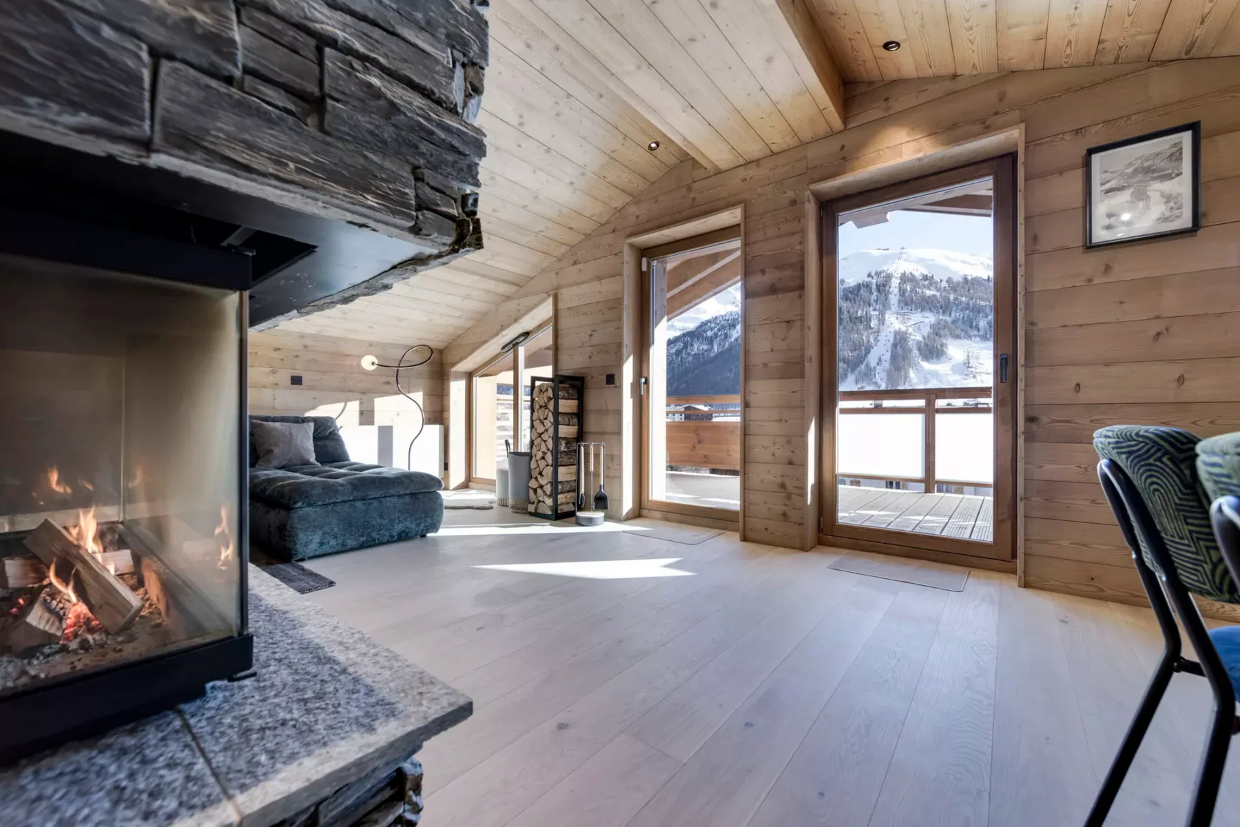 A wood-paneled living room with a fireplace and large windows overlooking snowy mountains.