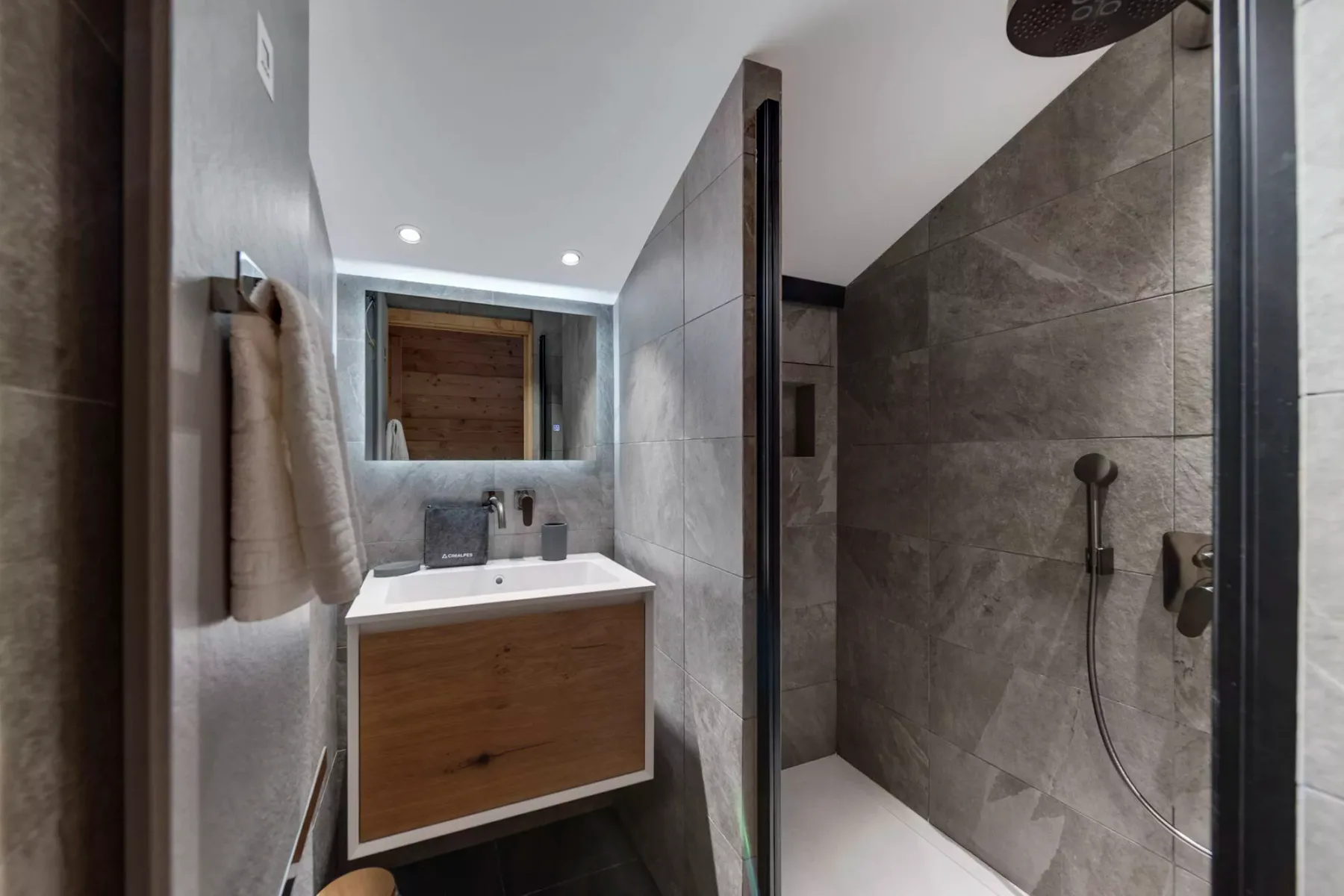 A modern bathroom with a wood-front vanity beside a walk-in shower.