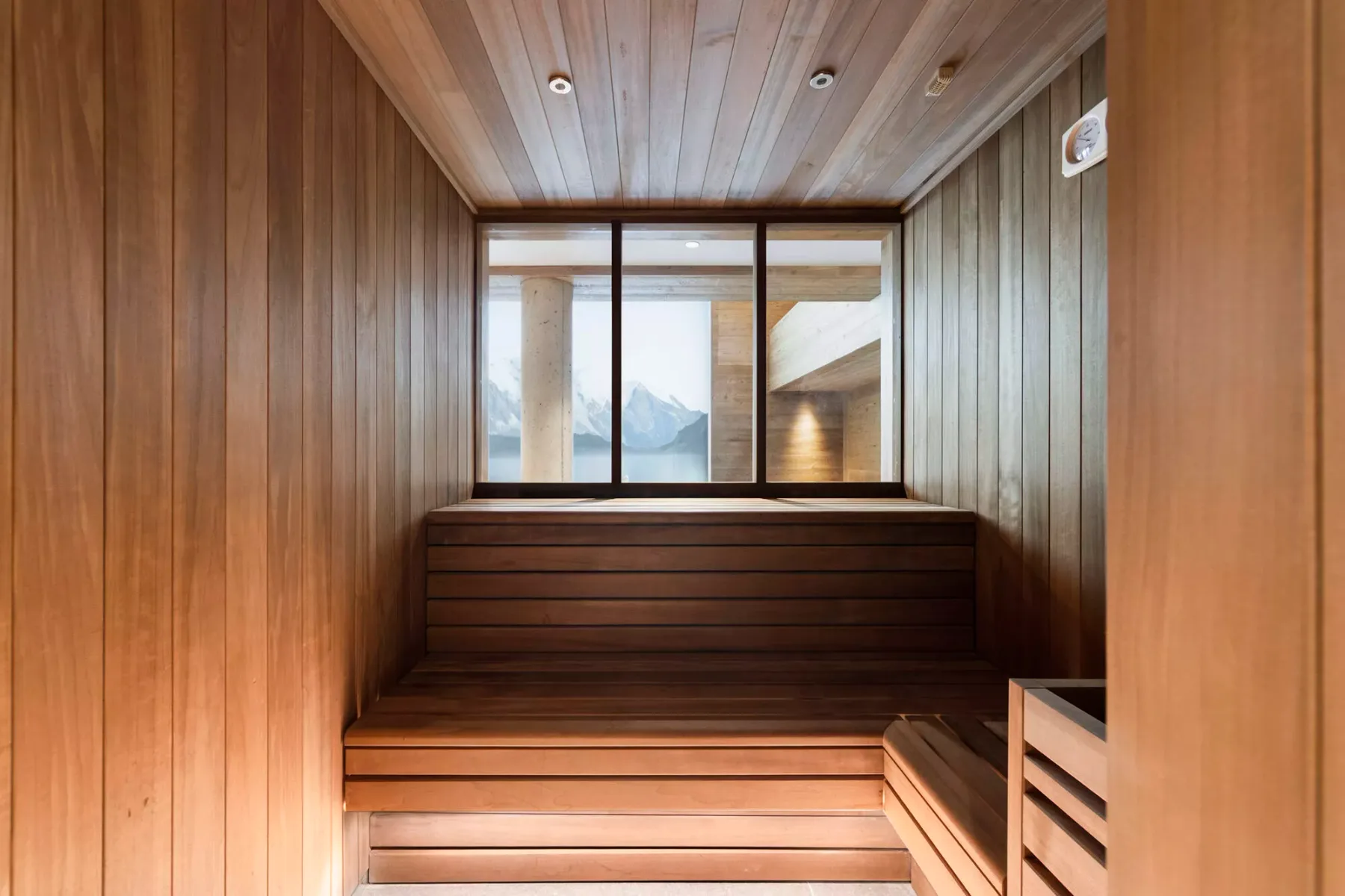 A wood-paneled sauna with tiered seating and a window overlooking mountains.