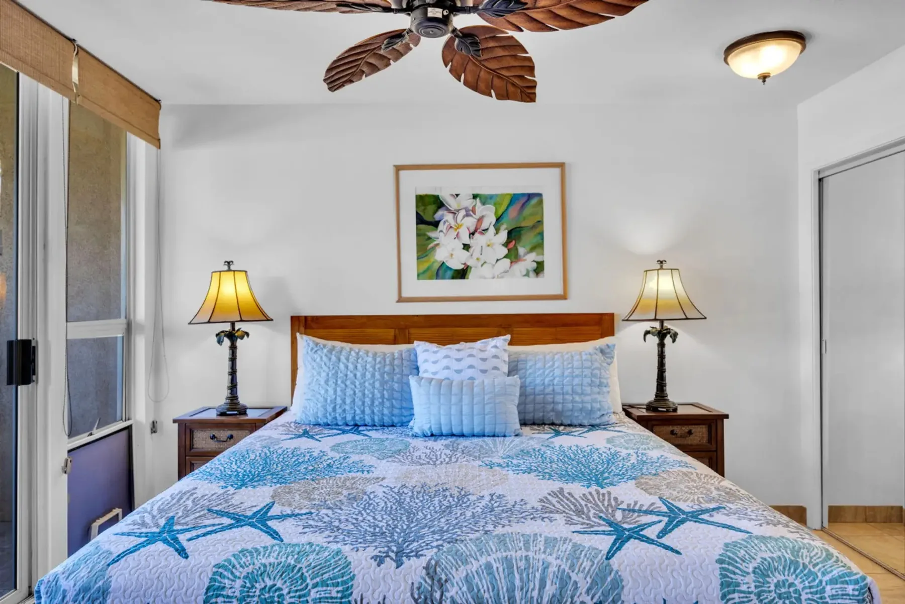 Un dormitorio con una cama vestida con ropa de cama azul y blanca bajo un cuadro floral.