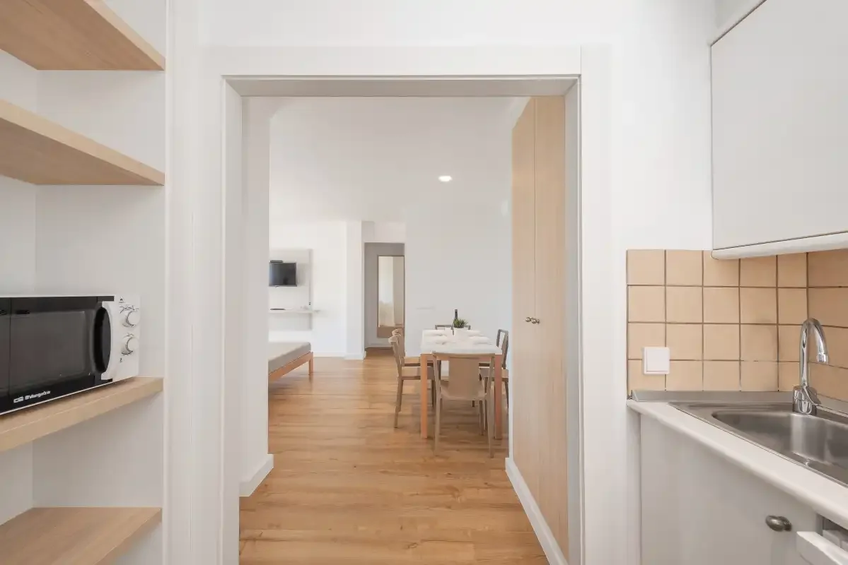 A bright kitchen opens through a doorway to a dining area with a wooden table.