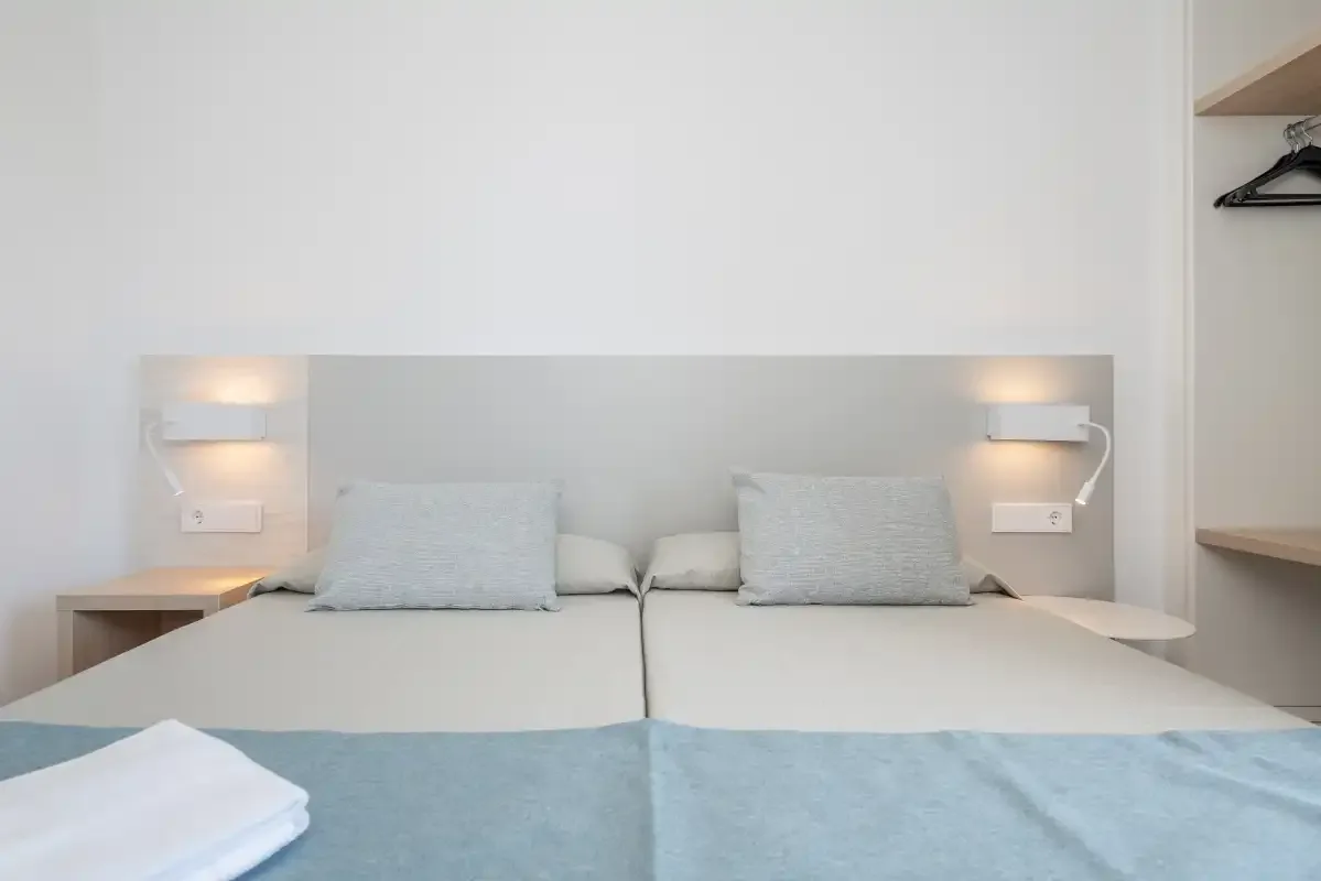 A bedroom with two beds, bedside lights, and folded towels.