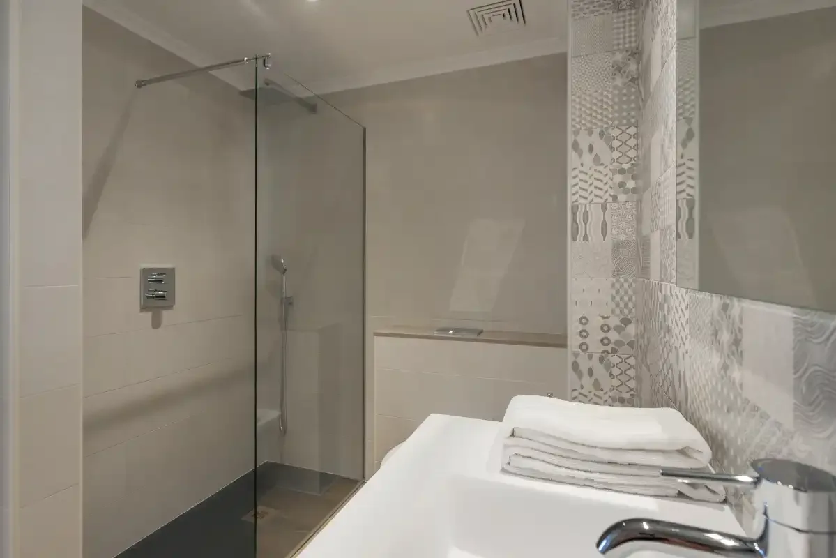 A modern bathroom with a glass shower and folded towels on the counter.