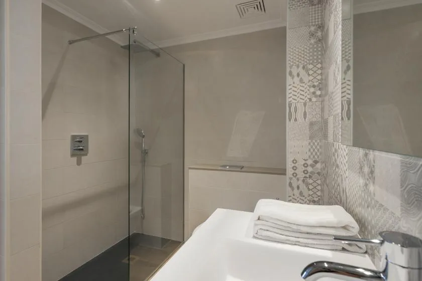 A tiled bathroom with a glass shower and folded towels on the counter.