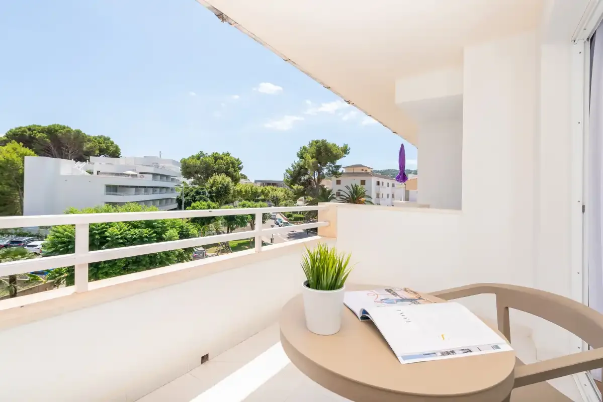 A bright balcony seating area with a potted plant and views of nearby buildings.