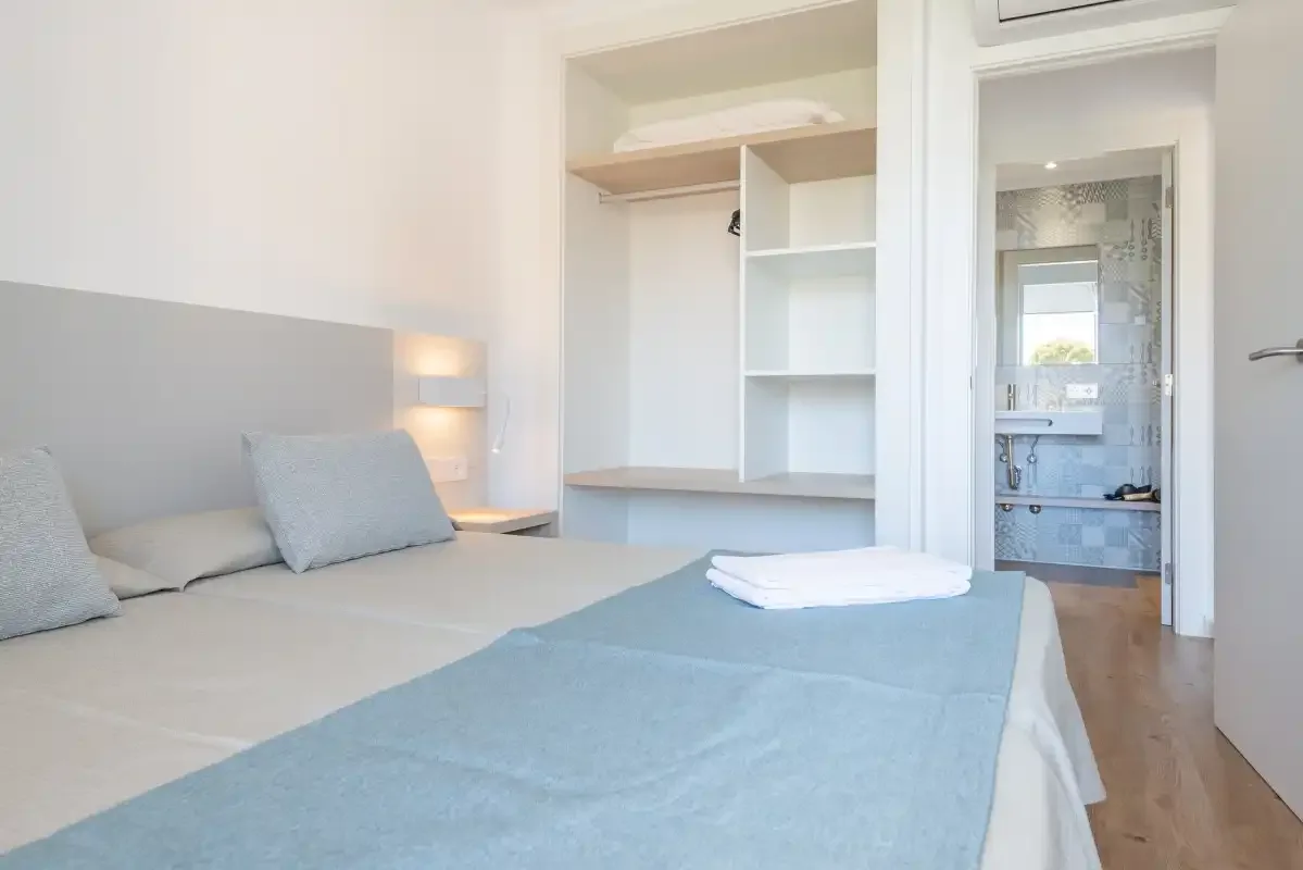 A bright bedroom with a bed, built-in shelving, and an open doorway to the bathroom.