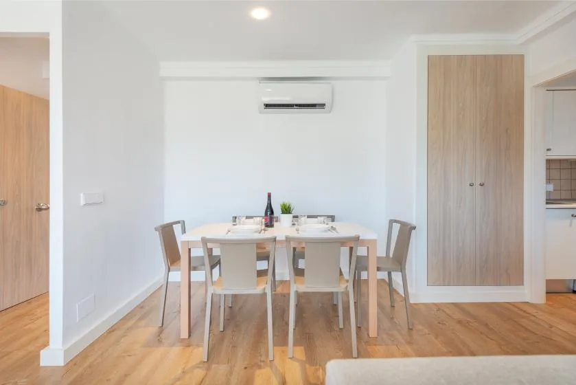 A dining area with a table and chairs sits against a white wall.