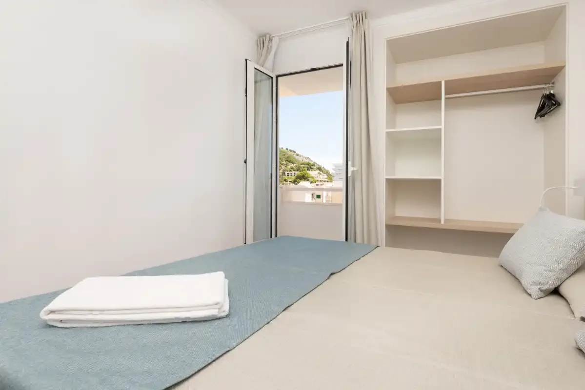 A bedroom with a bed and built-in open shelving beside an open balcony door.
