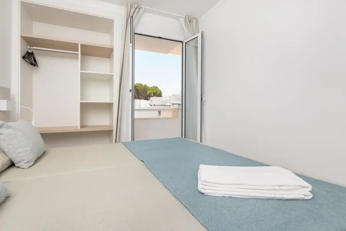 A bedroom with a bed beside an open window and built-in shelving.