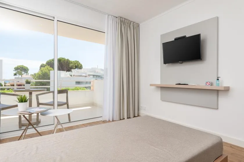 A bedroom with a bed, a wall-mounted television, and sliding glass doors opening onto a balcony.