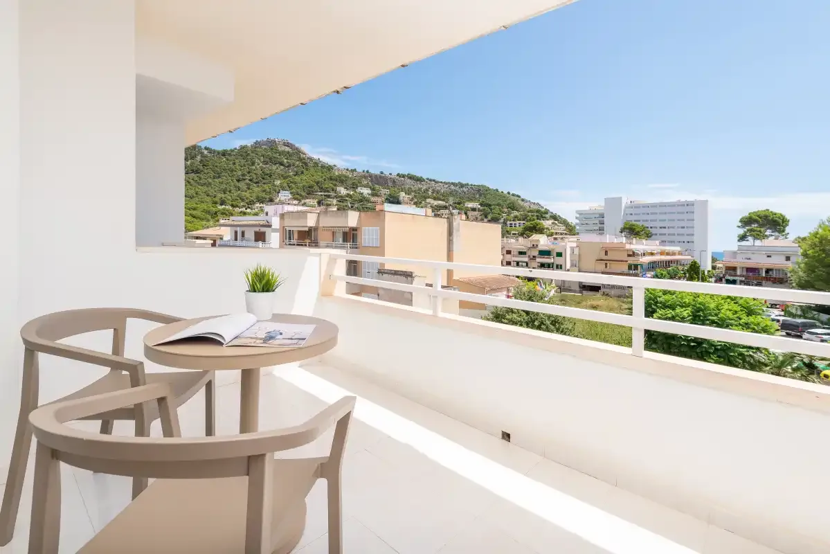 A balcony seating area overlooks nearby buildings and a green hillside.