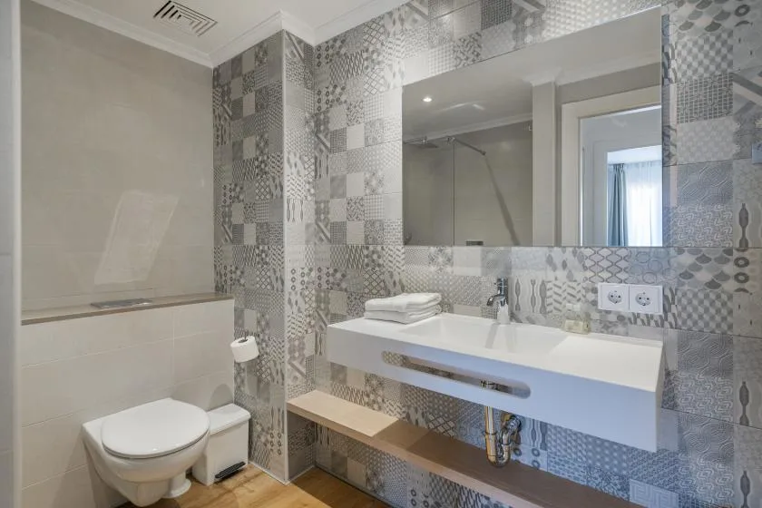 A bathroom with a wall-mounted sink, mirror, and patterned tile.