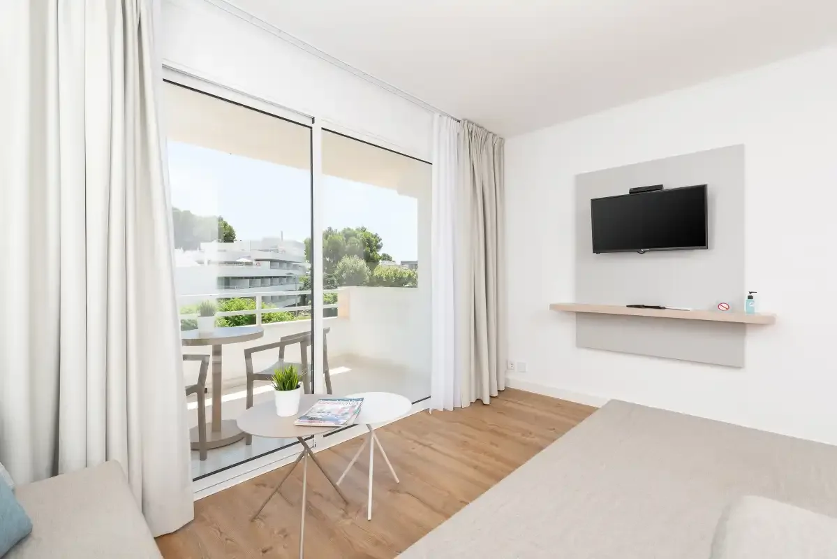 A bright bedroom with a wall-mounted television and sliding glass doors opening onto a balcony.