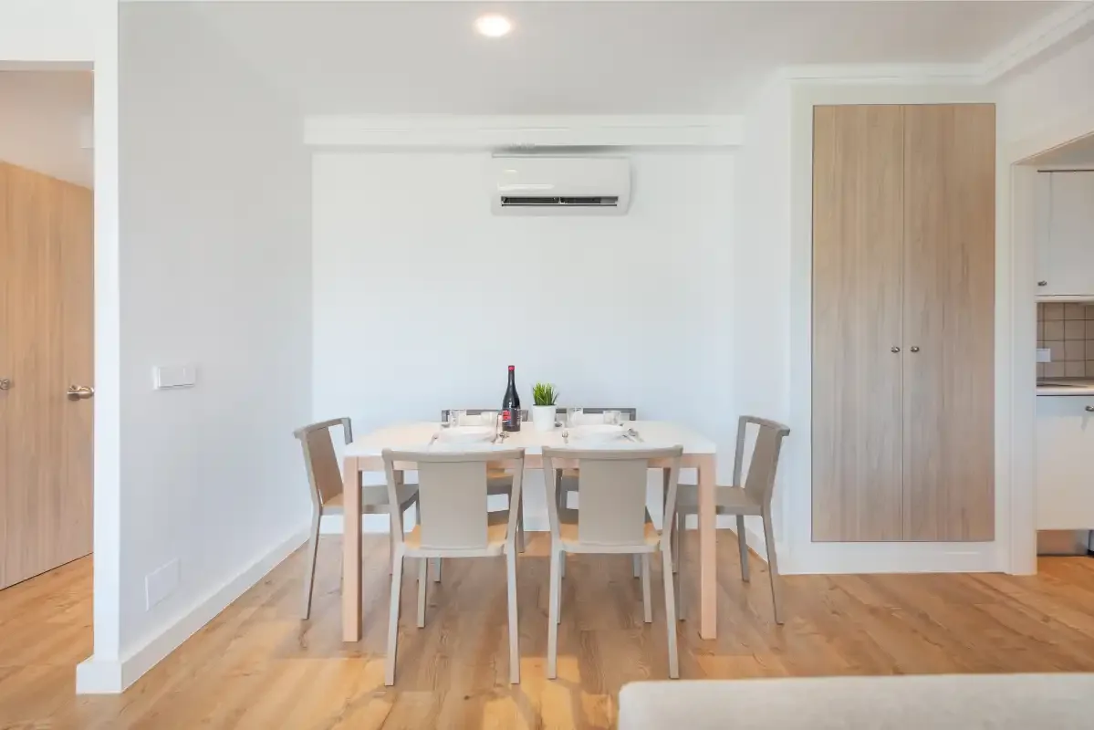 A dining area with a table and chairs beneath a wall-mounted air conditioner.