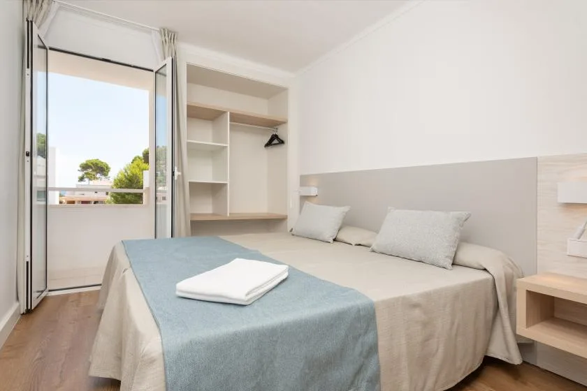 A bright bedroom with a neatly made bed and an open balcony door.
