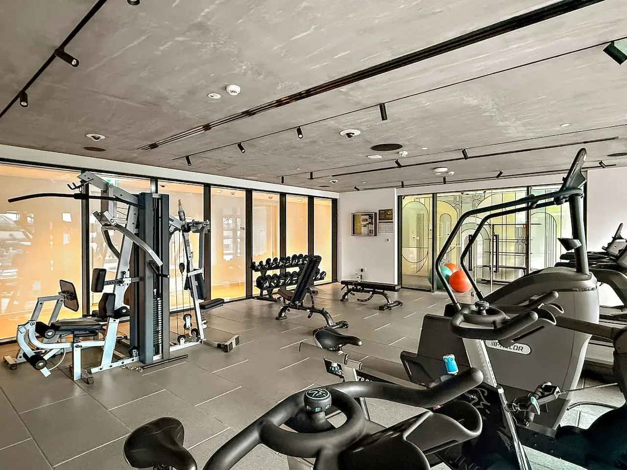 Un gimnasio con máquinas de ejercicio y pesas junto a grandes ventanales.