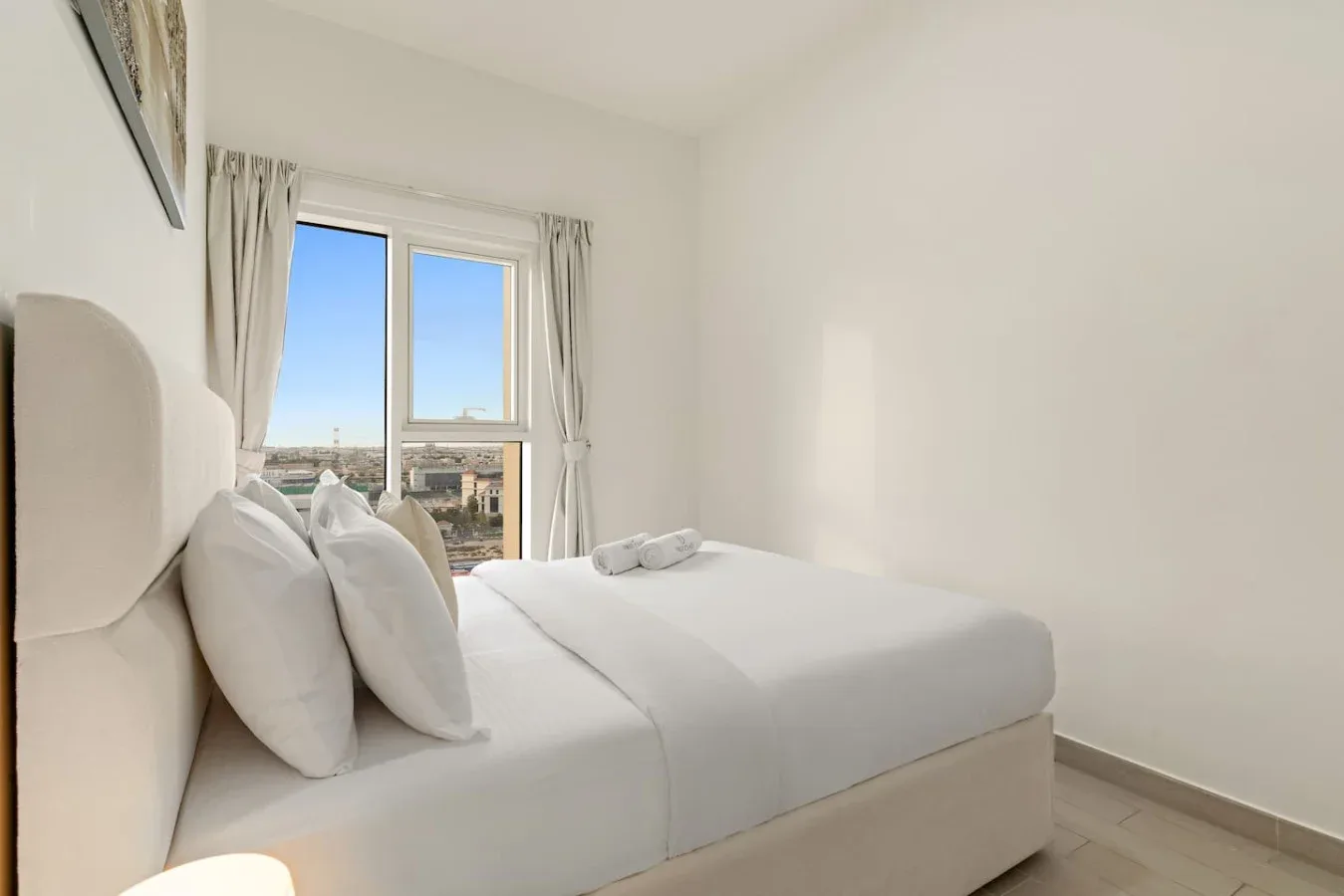 A bright bedroom with a neatly made bed beside a window.