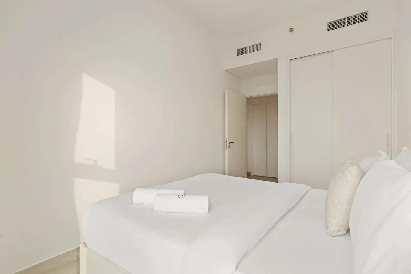 A bright bedroom with white bedding and a towel folded on the bed.