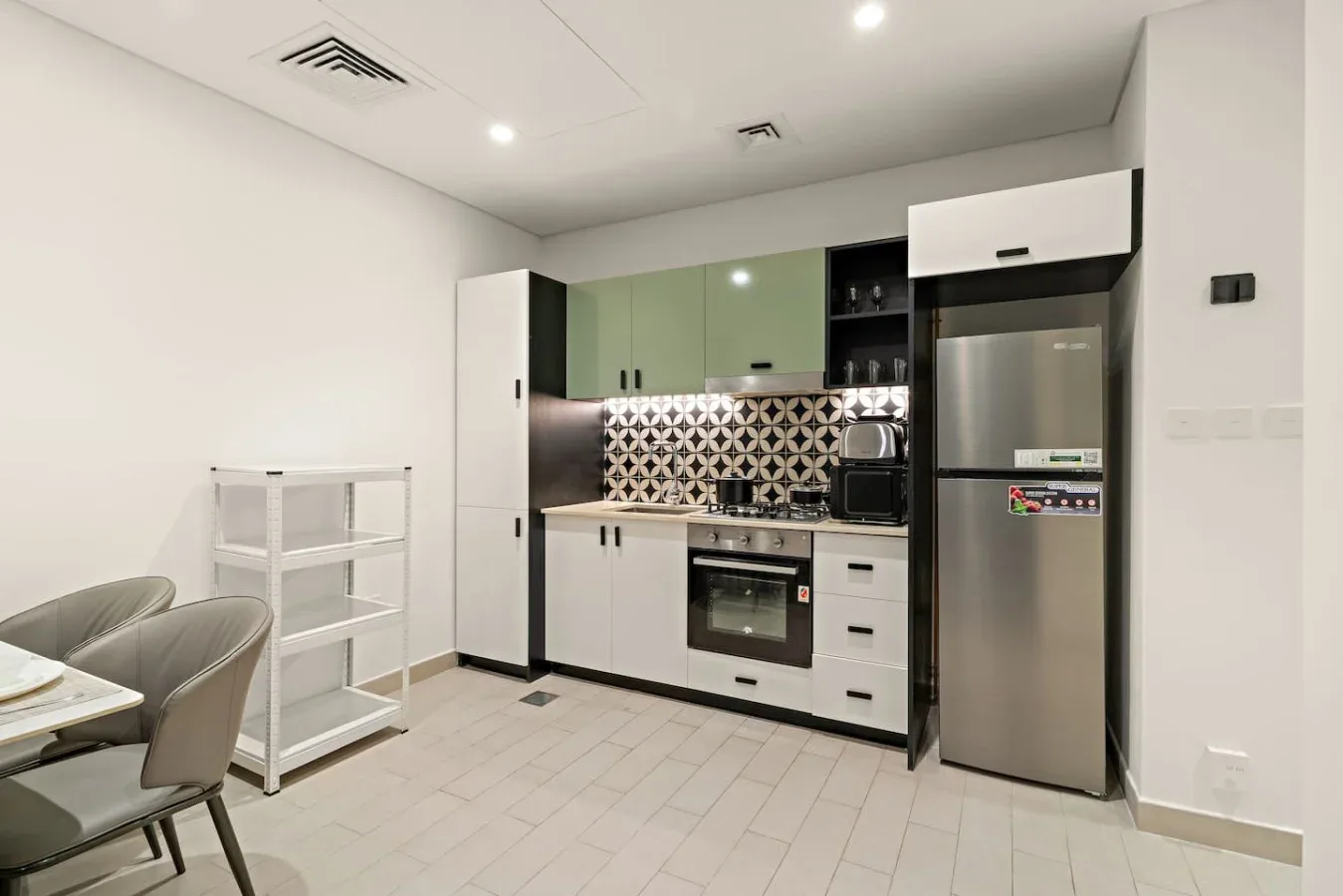 A compact kitchen with green cabinets, a stainless steel refrigerator, and a small dining area.