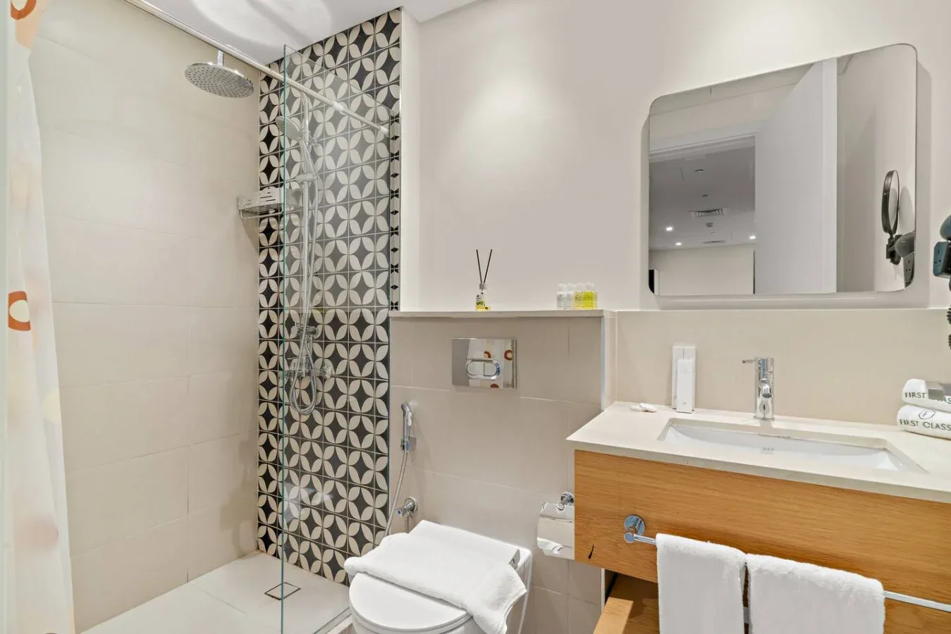 A bright bathroom with a glass shower, patterned wall tiles, and a wood-front vanity.