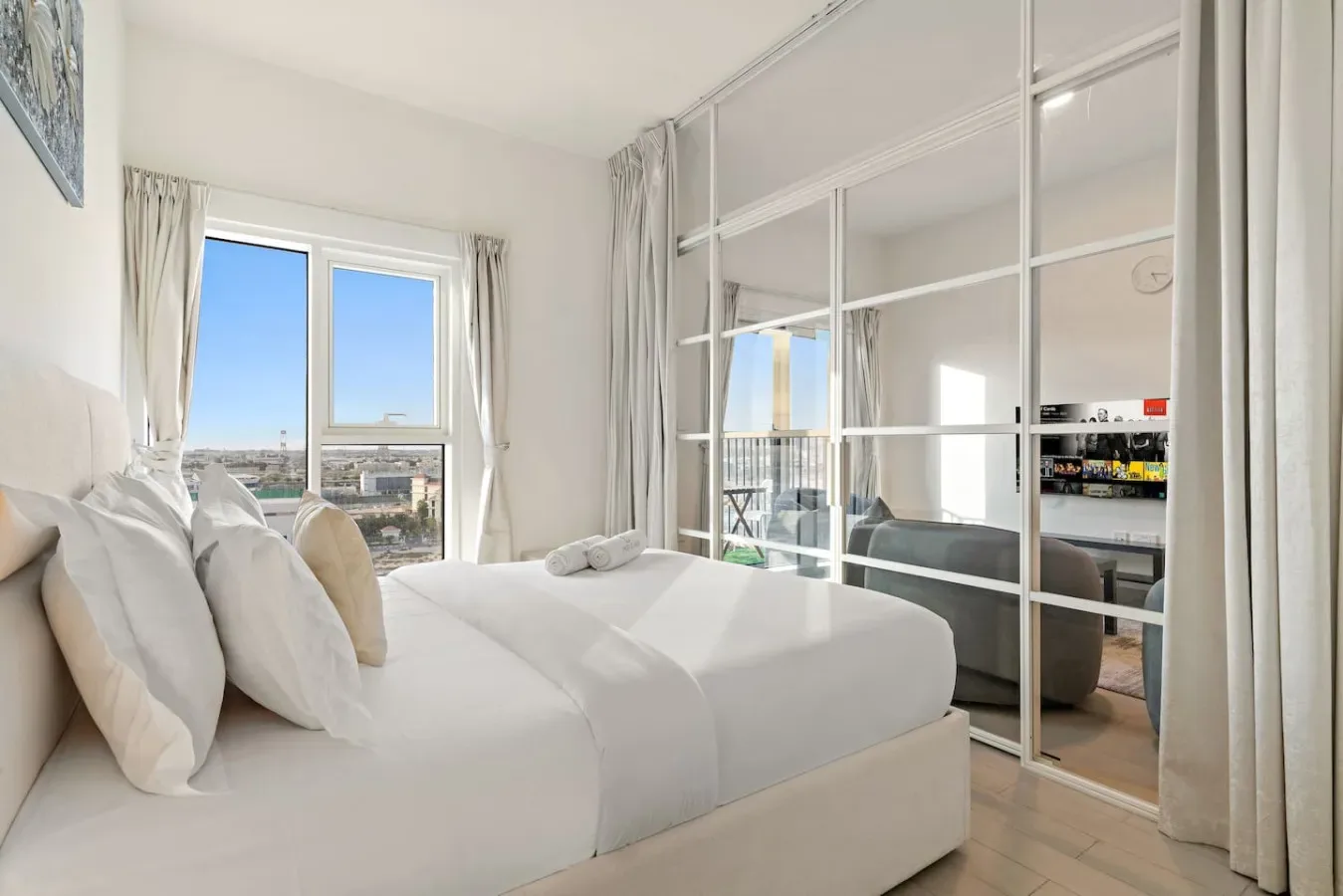 A bright bedroom with a neatly made bed beside mirrored sliding panels.