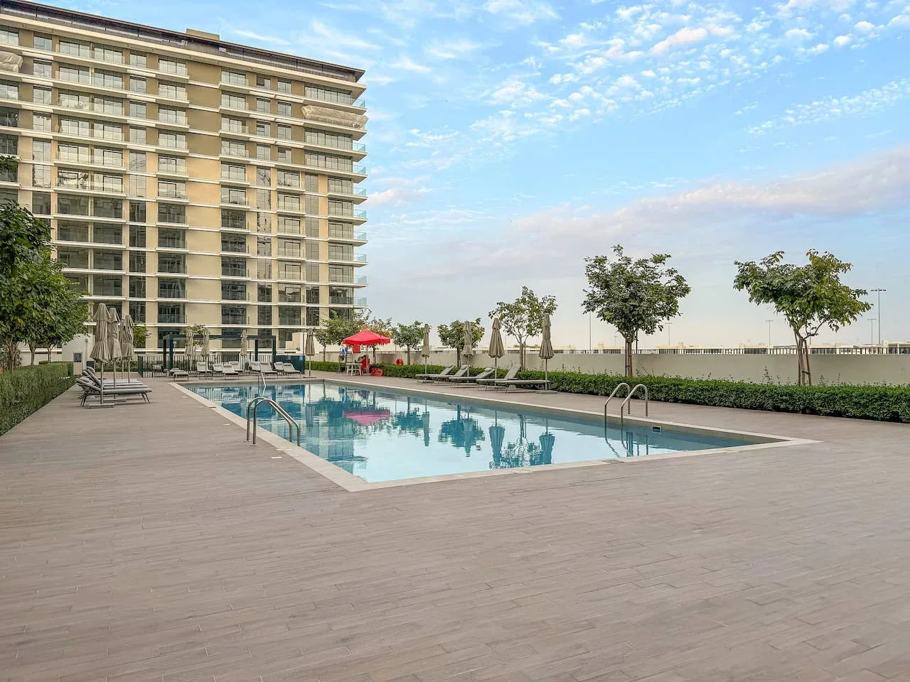 An outdoor swimming pool beside a multi-story building, with trees along the far side.
