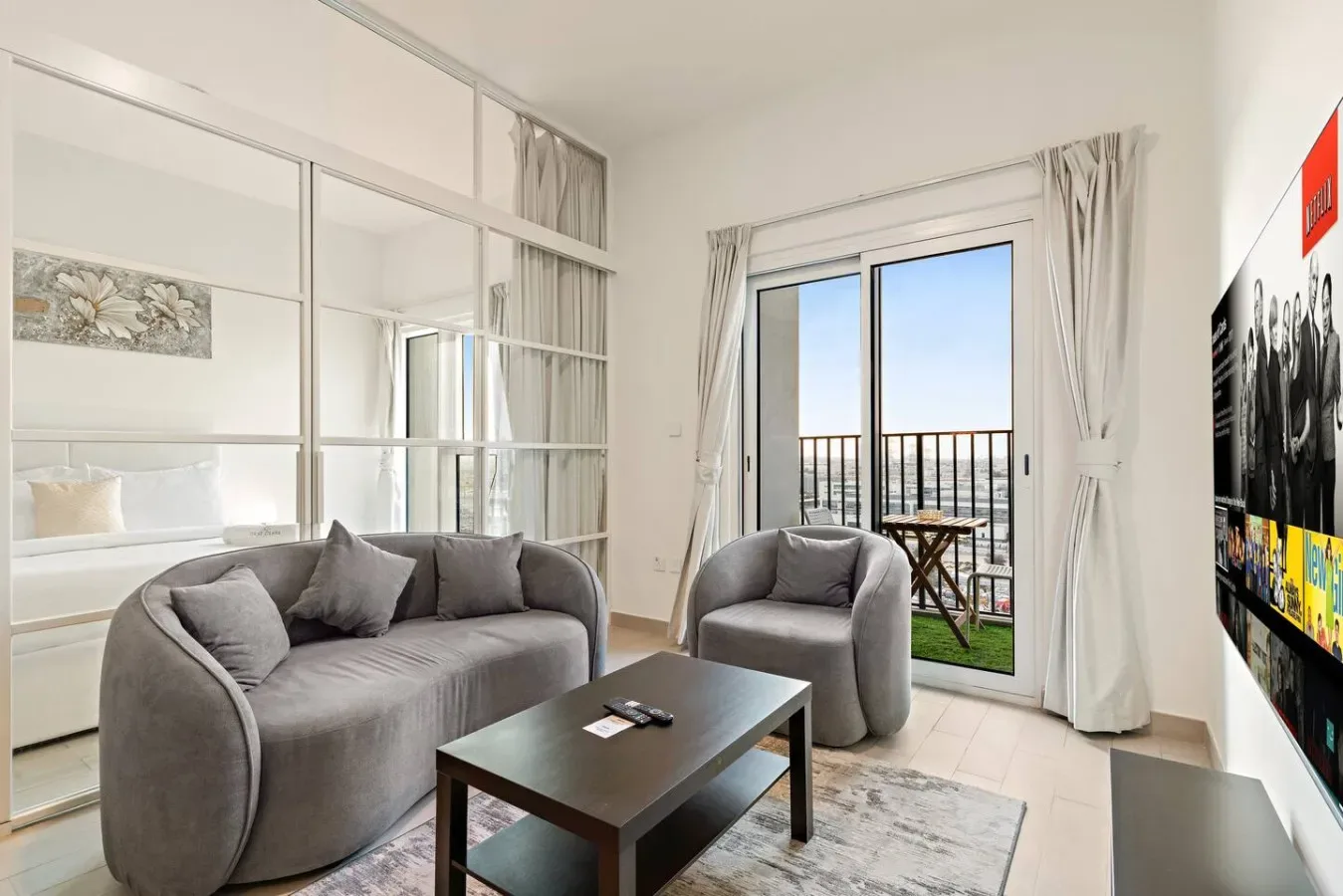 A bright living room with gray seating and glass doors opening onto a balcony.