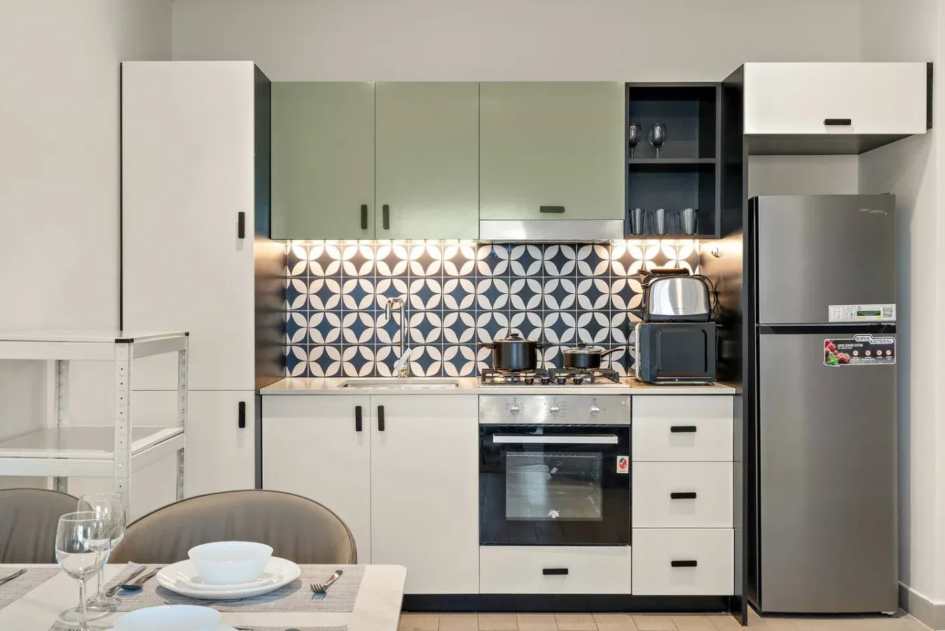 A modern kitchen with green cabinets, patterned backsplash, and stainless steel appliances.