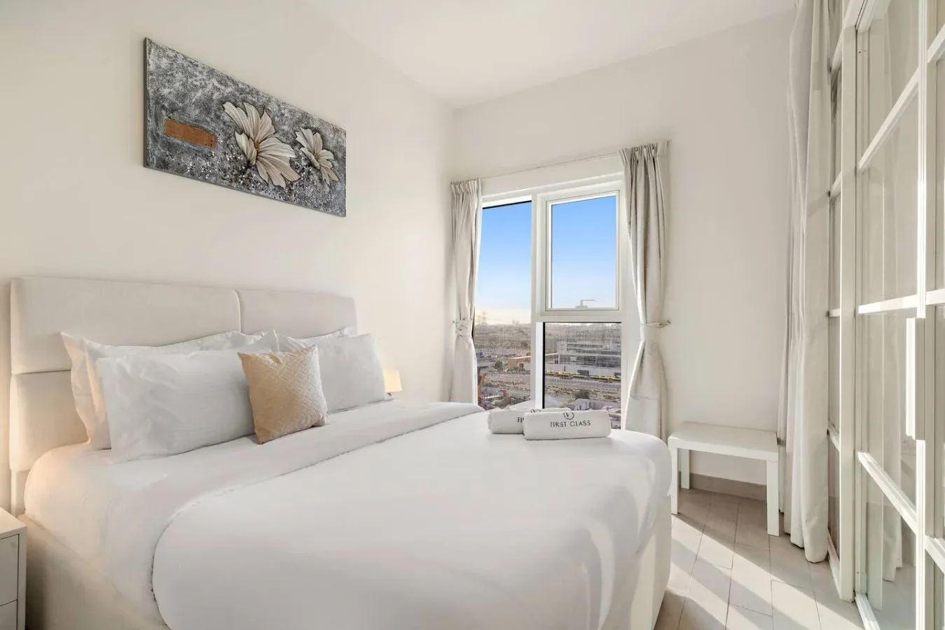 A bright bedroom with a neatly made bed beside a large window.