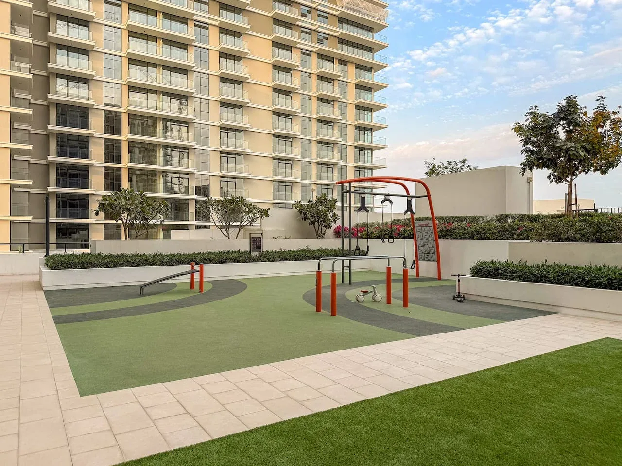 An outdoor playground with climbing equipment sits beside a landscaped apartment building.