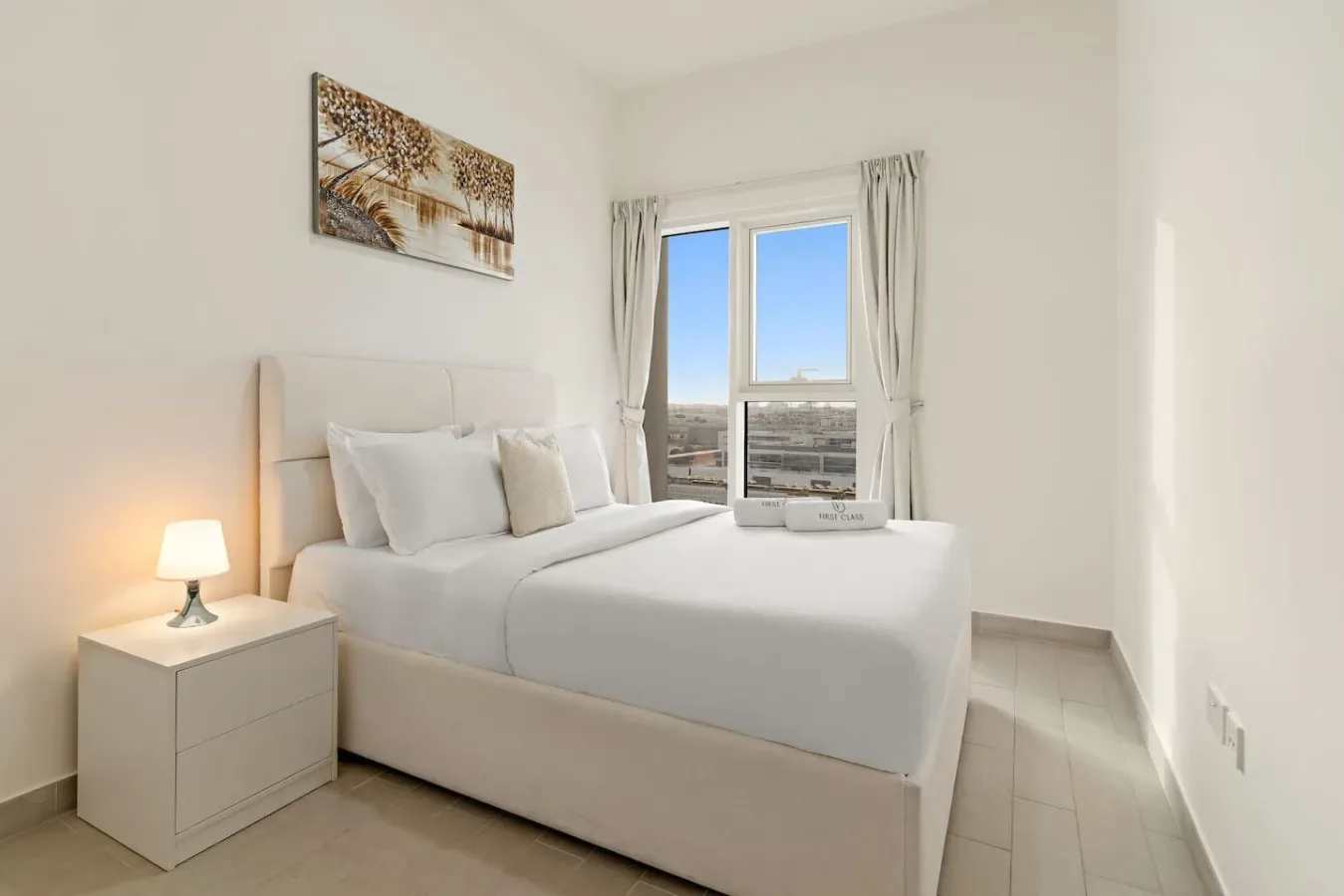 A bright bedroom with a neatly made bed beside a window.