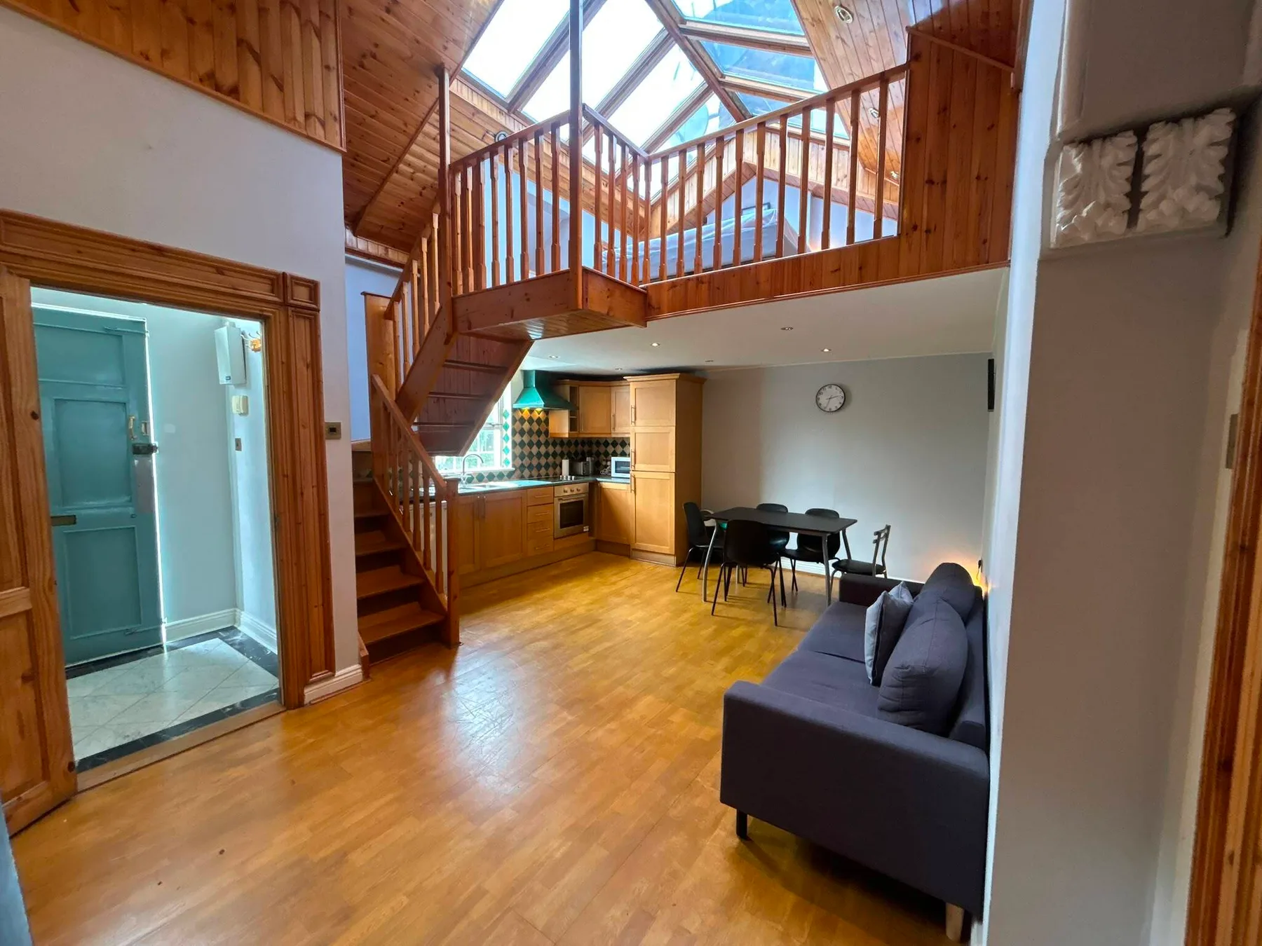 A wood-floored living area with a dining table beneath a skylit loft.