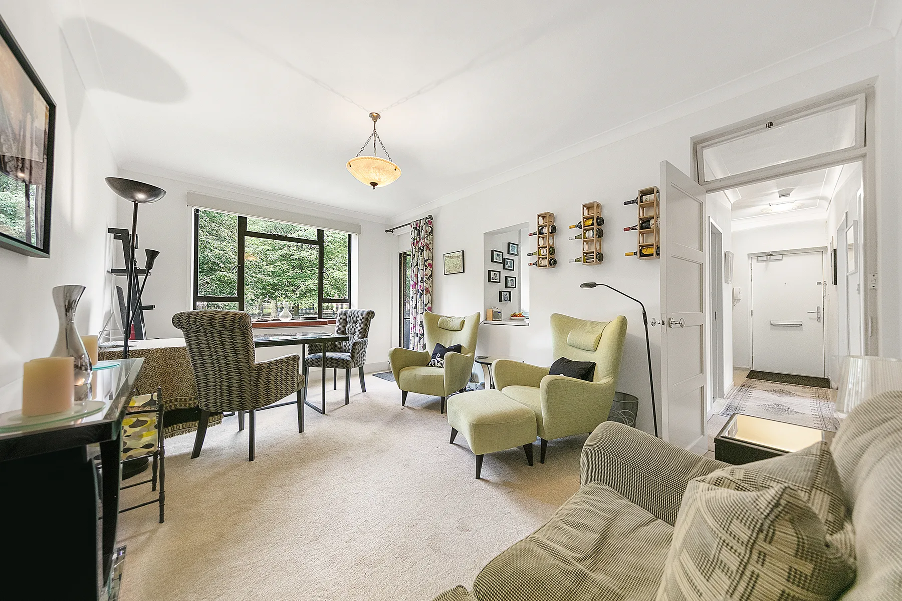 A bright living room has armchairs, a dining table, and a large window.