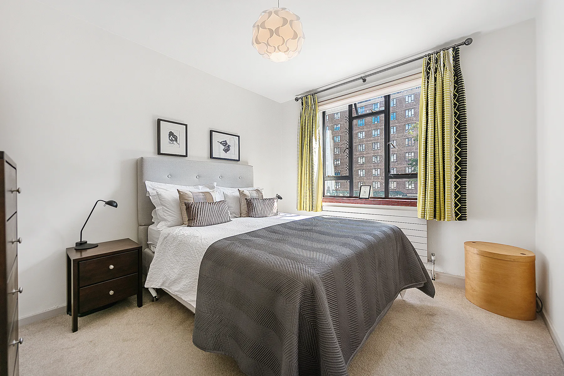 A bright bedroom with a bed beneath a large window with patterned curtains.