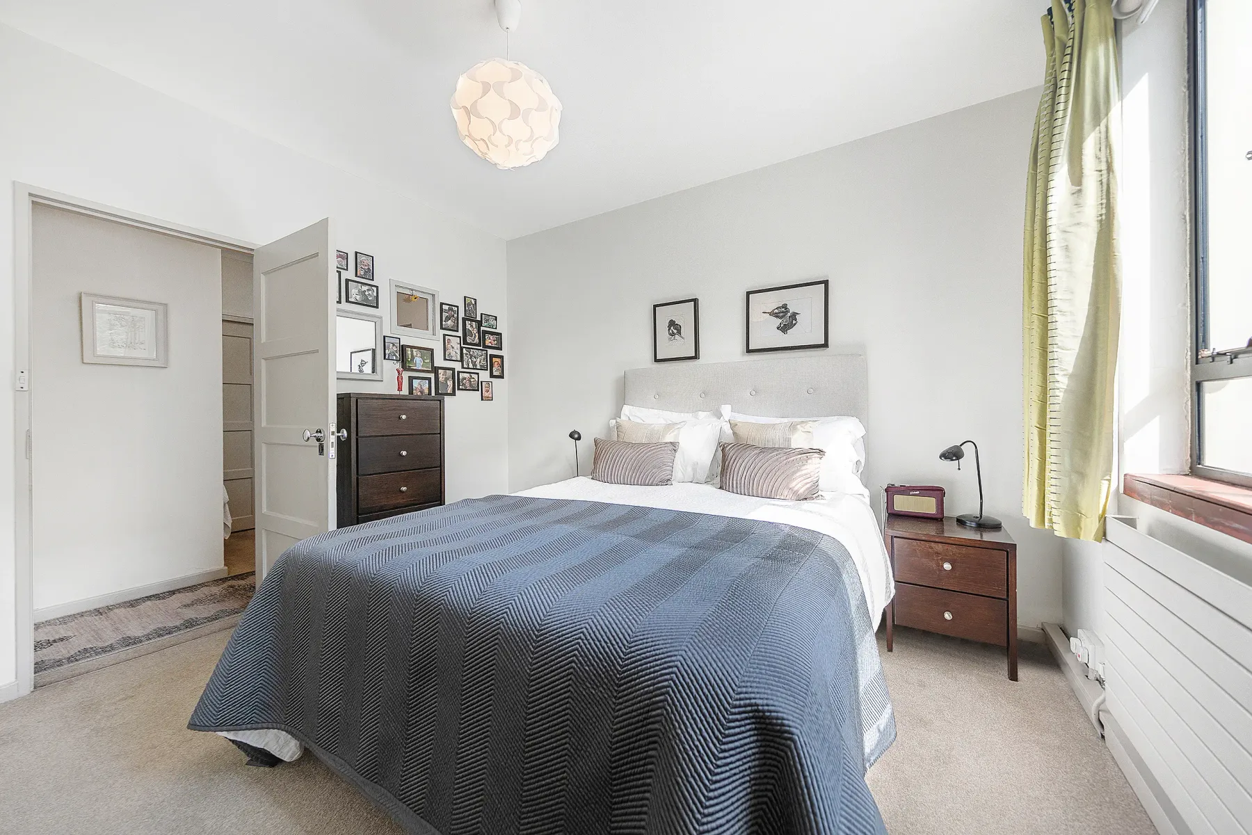 A bedroom with a neatly made bed, framed artwork, and bedside tables.