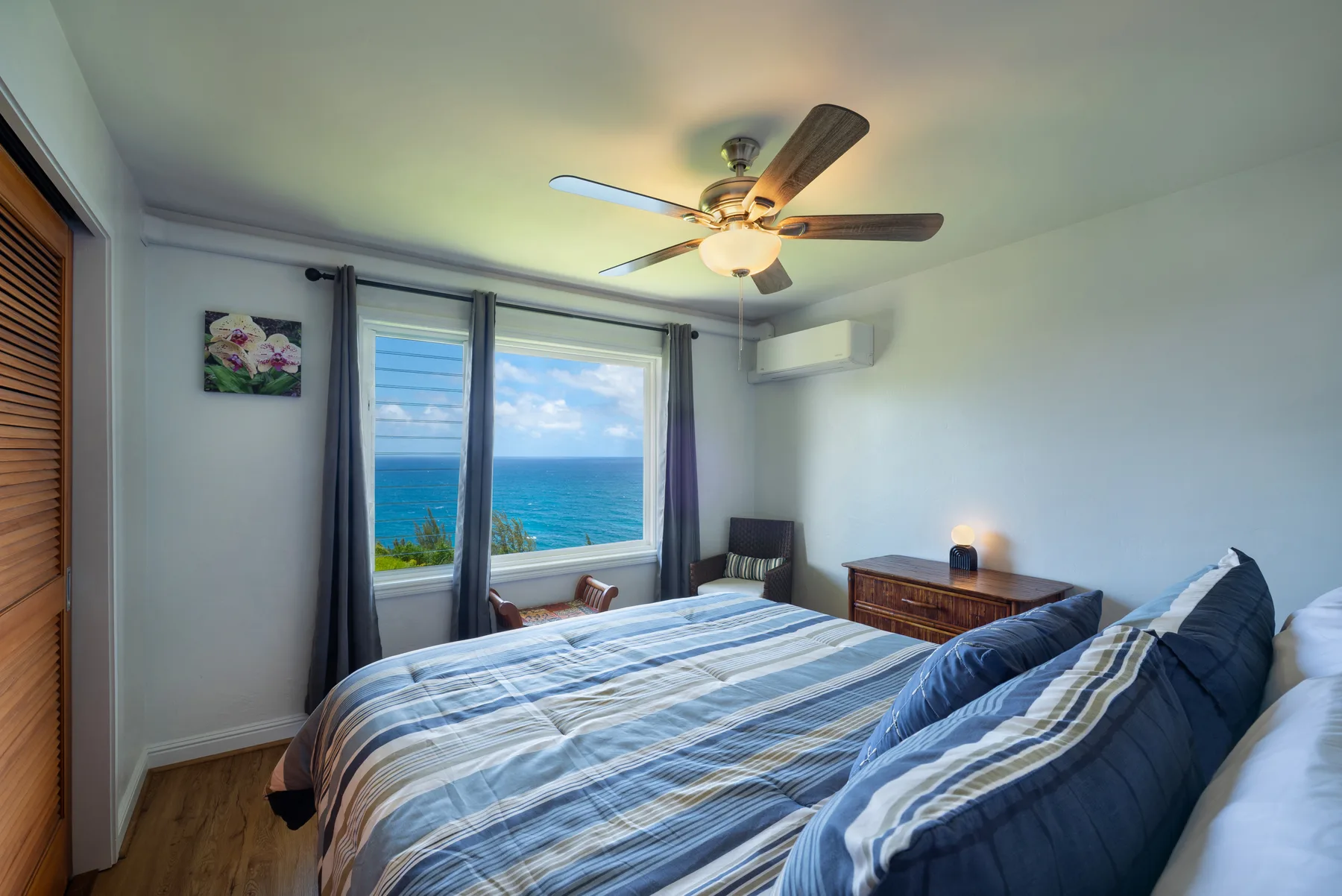 Un dormitorio con ropa de cama a rayas azules y una ventana con vista al mar.