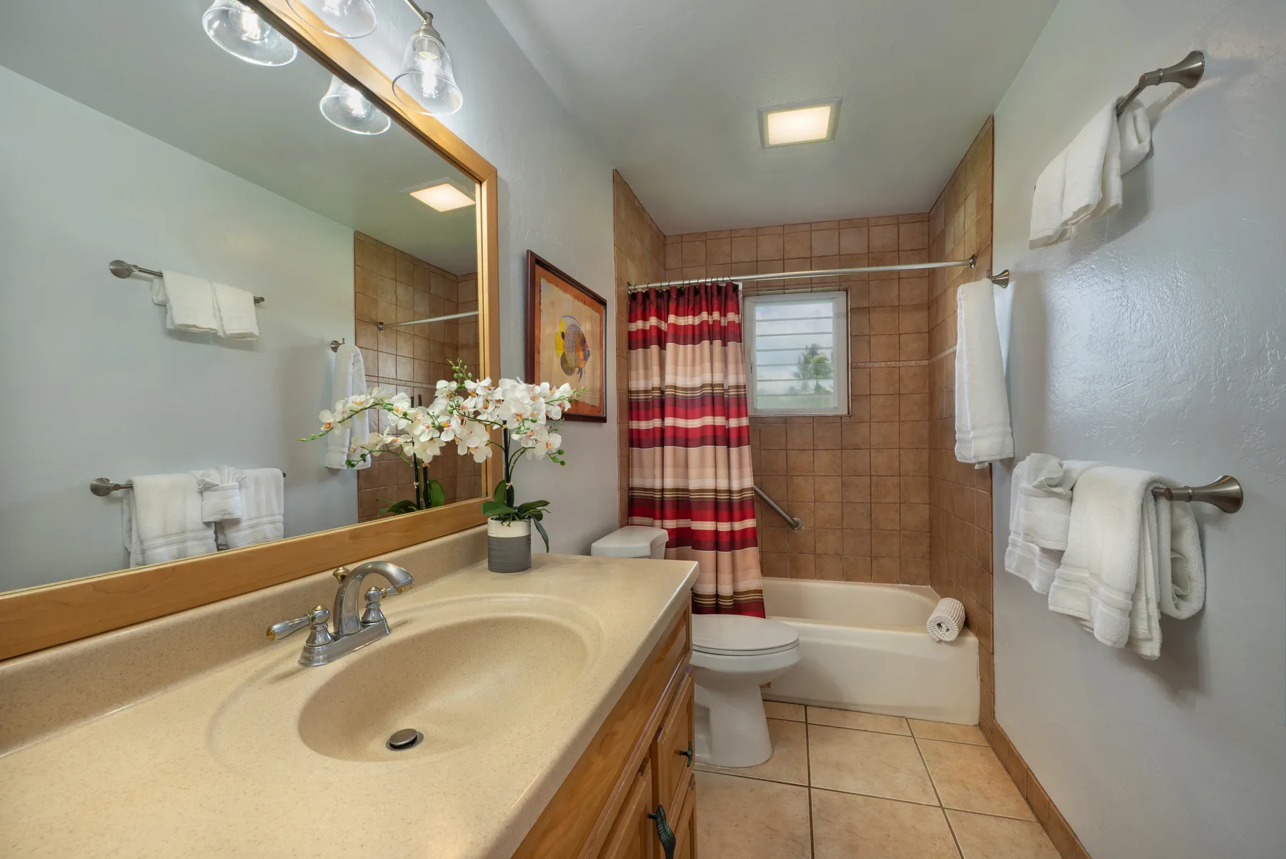 Un baño con lavabo y mueble, inodoro y bañera detrás de una cortina de ducha a rayas.