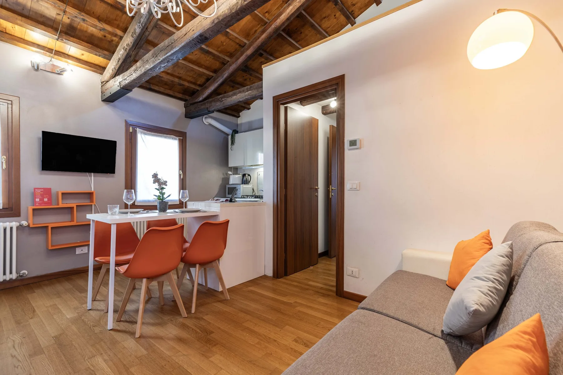 Una pequeña sala con comedor y barra de cocina, bajo vigas de madera expuestas.