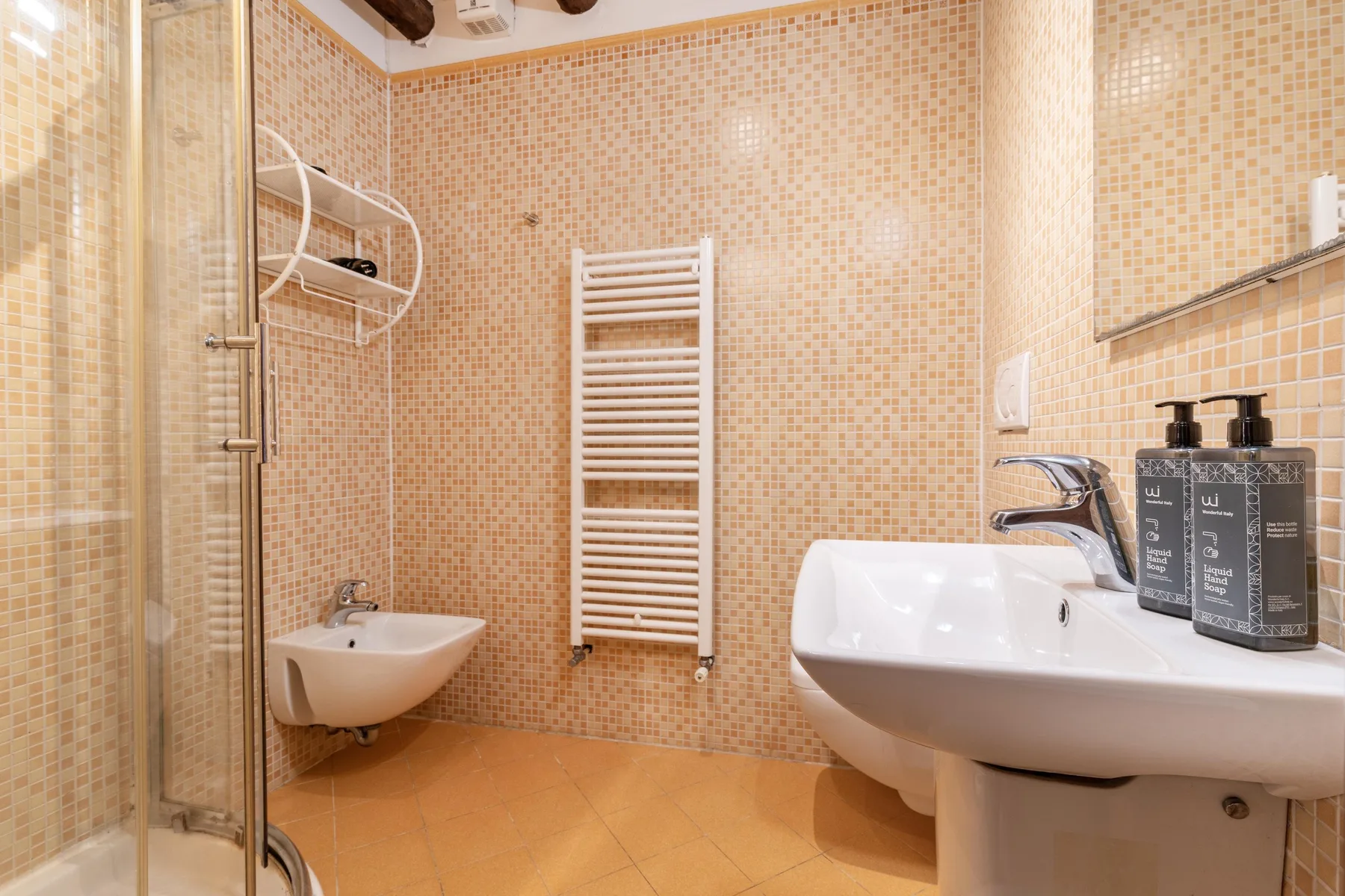 Un baño con azulejos, ducha, lavabo de pared y toallero calefactable.