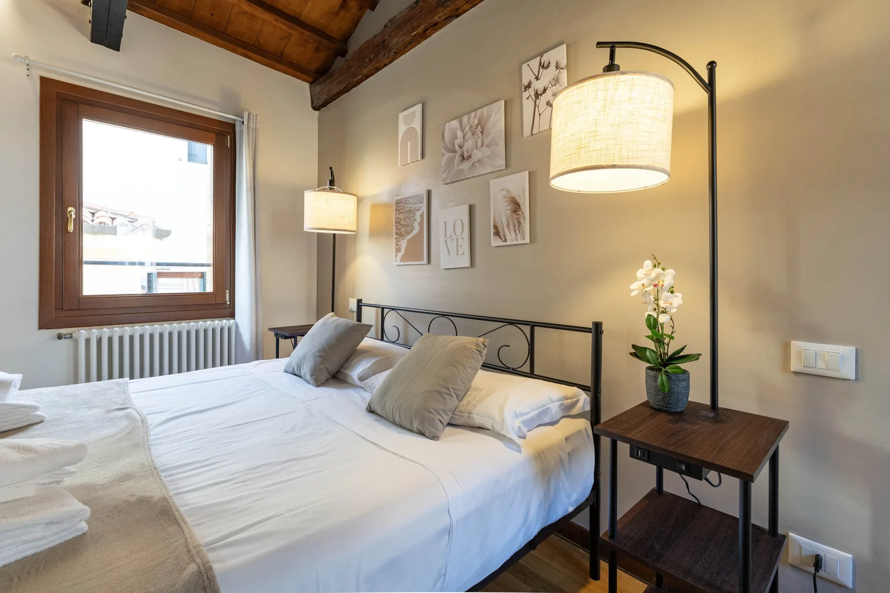 Un dormitorio con una cama hecha, cuadros en la pared y una mesa de noche.