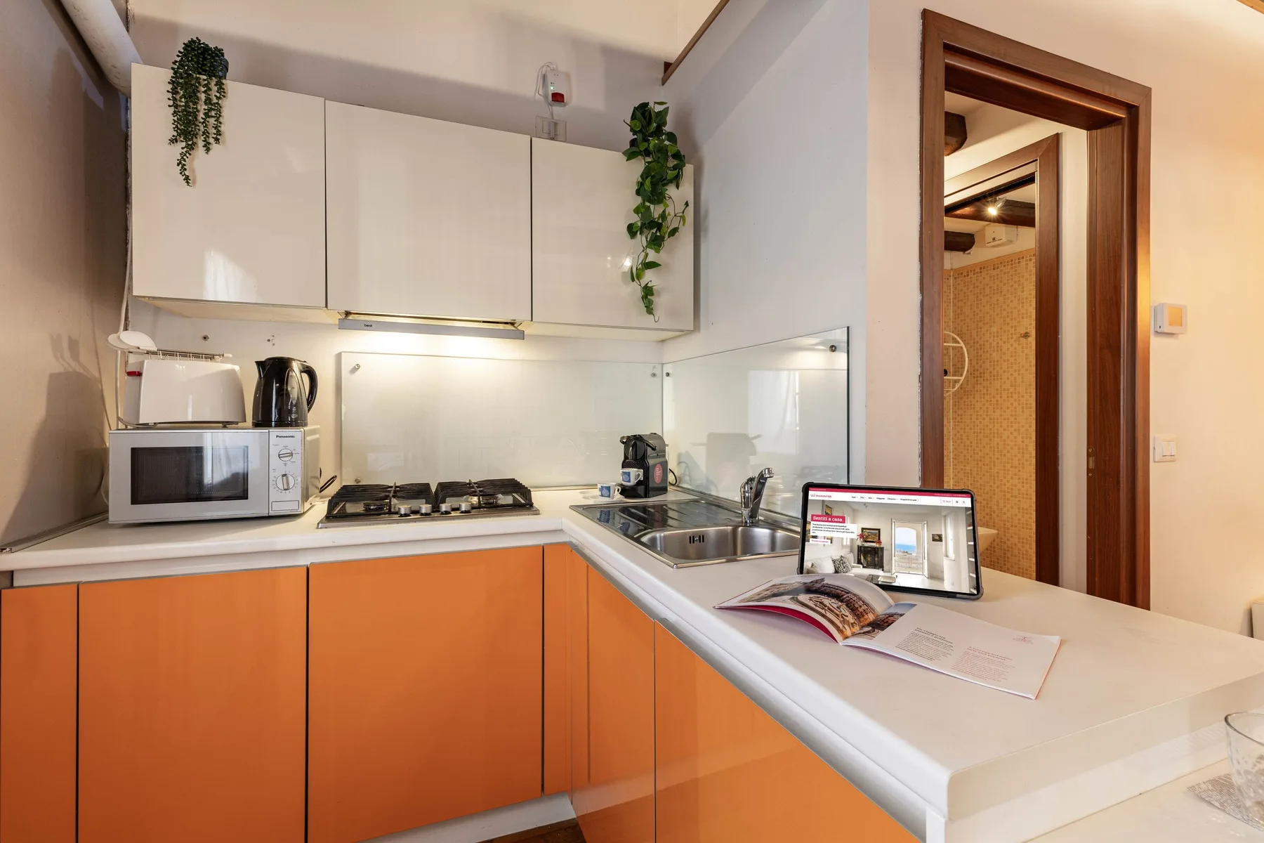 Una cocina compacta con gabinetes inferiores naranjas, una placa de cocción y un fregadero.