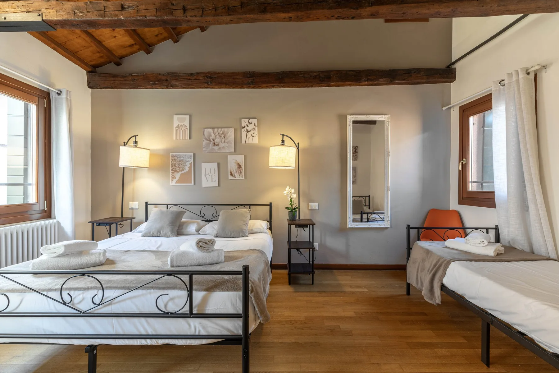 Un dormitorio con una cama grande y otra más pequeña bajo vigas de madera vistas.