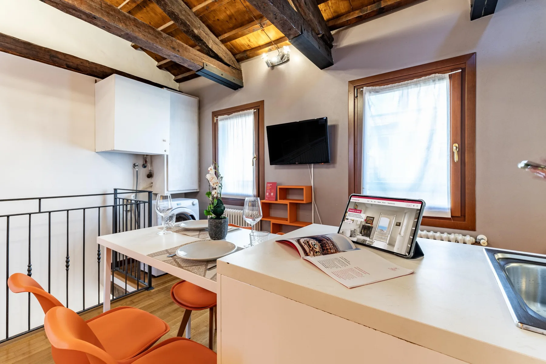 Un interior tipo loft luminoso con mesa de comedor, asientos naranjas y vigas de madera expuestas.
