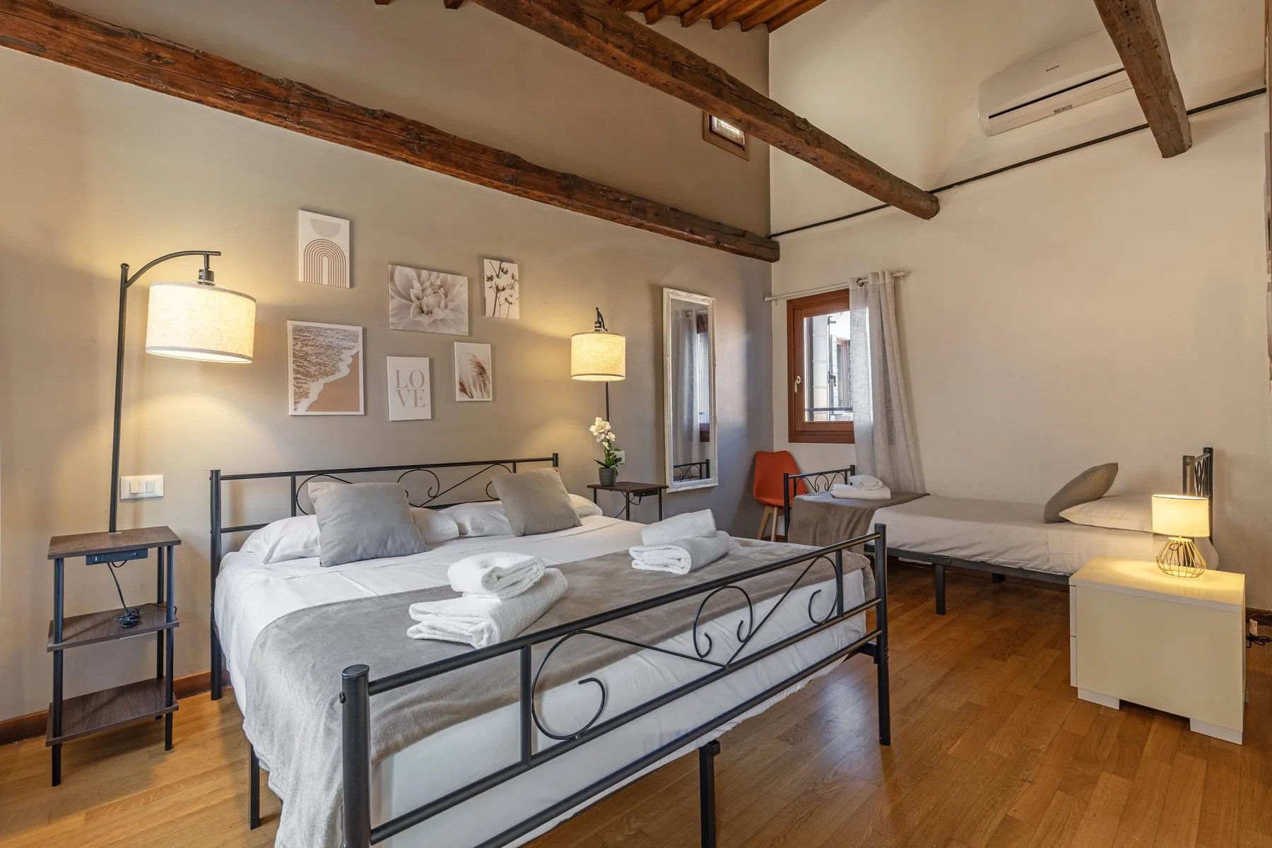 Un dormitorio con una cama grande, una zona de estar separada y vigas de madera a la vista en el techo.
