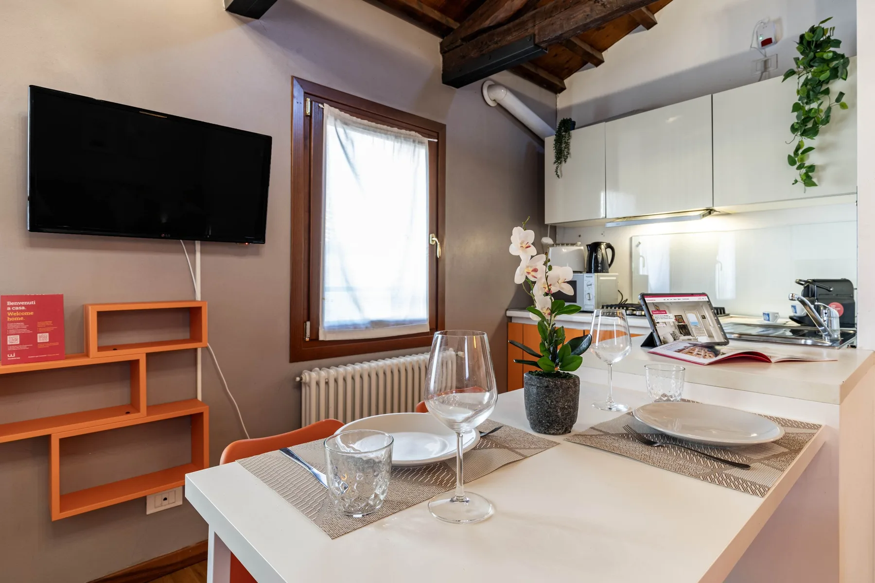 Un comedor con la mesa puesta junto a una cocina compacta y una ventana.