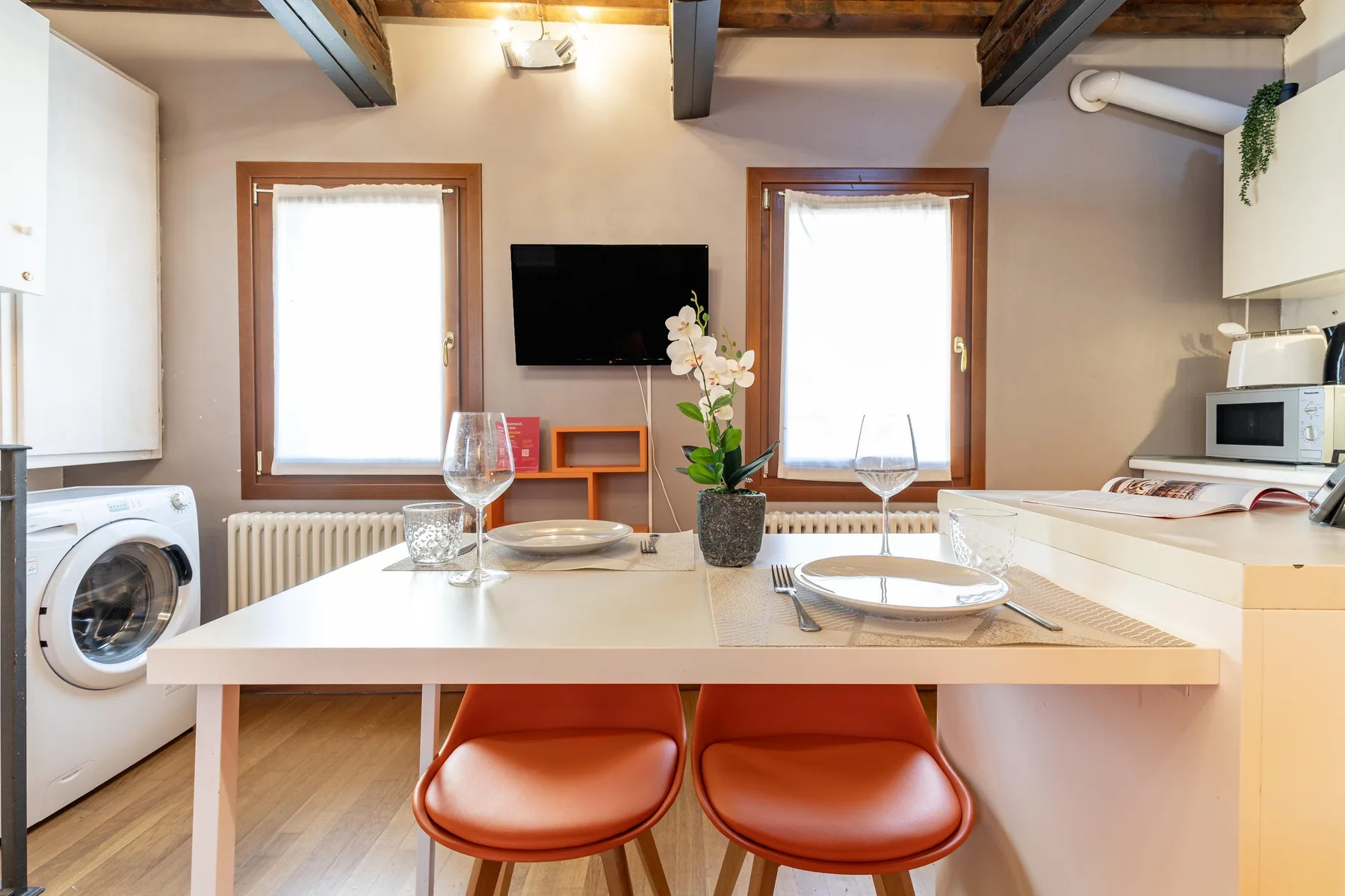 Una cocina compacta con comedor, una mesa, dos asientos y un televisor en la pared.