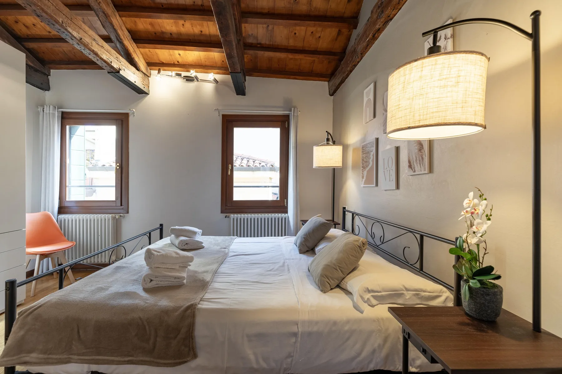 Un dormitorio con una cama bajo vigas de madera vistas y dos ventanas.